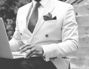 A man wearing a white suit with a laptop on his knees.